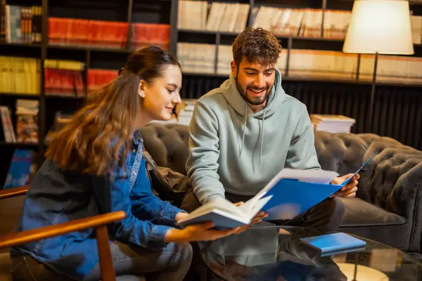 İki odaklanmış öğrenci sessiz bir kütüphane ortamında birlikte okuyorlar, bir klasörden içeriği okuyup tartışıyorlar.. 