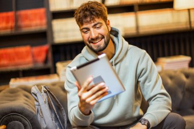 Odaklanmış bir erkek öğrenci sessiz bir kütüphane ortamında dijital tablet kullanıyor.. 