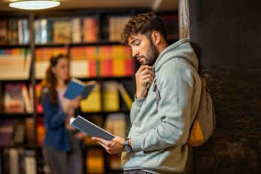 Genç bir erkek öğrenci sessiz bir kütüphane ortamında kitap okumaya derinden odaklanmıştır.. 