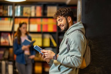 Genç bir erkek öğrenci sessiz bir kütüphane ortamında kitap okumaya derinden odaklanmıştır.. 