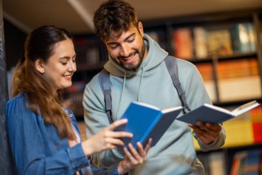 Erkek ve bayan öğrenci sessiz kütüphanede birlikte kitap okurlar..