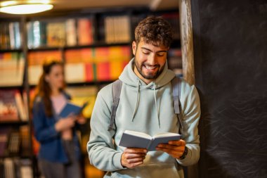 Genç bir erkek öğrenci sessiz bir kütüphane ortamında kitap okumaya derinden odaklanmıştır.. 