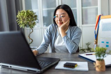Genç bir Taylandlı kadın evde çalışıyor, rahat bir ofis ortamında bilgisayarına odaklanmış..