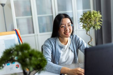 Genç bir Taylandlı kadın evde çalışıyor, rahat bir ofis ortamında bilgisayarına odaklanmış..