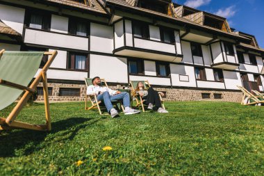 Genç bir adam ve kadın güneşli bir hafta sonu kaçışı sırasında bir dağ otelindeki şezlonglarda dinleniyorlar..