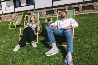 Genç bir adam ve kadın güneşli bir hafta sonu kaçışı sırasında bir dağ otelindeki şezlonglarda dinleniyorlar..