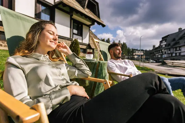 Genç bir adam ve kadın güneşli bir hafta sonu kaçışı sırasında bir dağ otelindeki şezlonglarda dinleniyorlar..