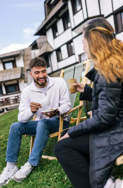 Genç bir adam ve bir kadın, hafta sonu kaçamağı sırasında şezlonglarda dinleniyorlar. Doğa ve temiz havayla çevrili olarak sıcak kahvenin ve ferahlatıcı meyve suyunun tadını çıkarırlar..