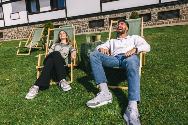 Genç bir adam ve kadın güneşli bir hafta sonu kaçışı sırasında bir dağ otelindeki şezlonglarda dinleniyorlar..