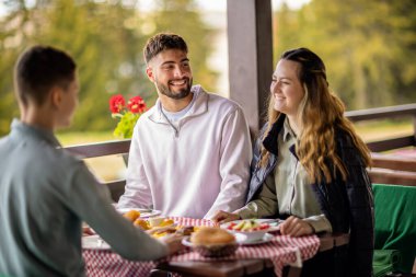 Erkek ve kız kardeşler açık bir bahar ya da sonbahar gününde bir dağ restoranının terasında öğle yemeği yiyorlar..