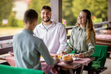 Erkek ve kız kardeşler açık bir bahar ya da sonbahar gününde bir dağ restoranının terasında öğle yemeği yiyorlar..
