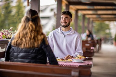 Genç bir çift dışarıda, dağlarda yemek yiyor.