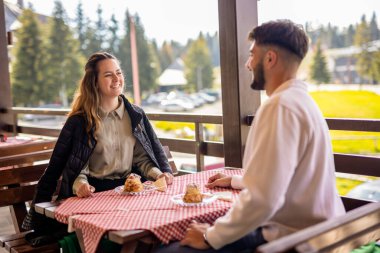 Genç bir çift, bir dağ restoranının terasında krema dolu profiterollerin tadını çıkarıyor.