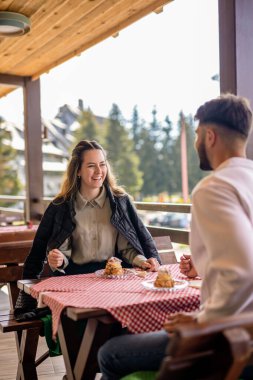 Genç bir çift, bir dağ restoranının terasında krema dolu profiterollerin tadını çıkarıyor.