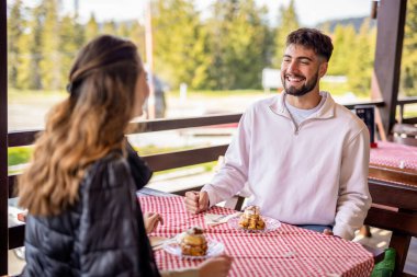 Genç bir çift, bir dağ restoranının terasında krema dolu profiterollerin tadını çıkarıyor.