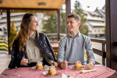 Mutlu erkek ve kız kardeşler güneşli bir restoranın terasında krema dolu profiterollerin tadını çıkarıyorlar..