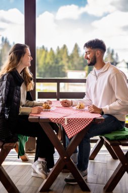 Genç bir çift, bir dağ restoranının terasında krema dolu profiterollerin tadını çıkarıyor.