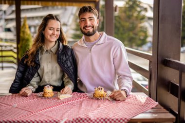 Genç bir çift, bir dağ restoranının terasında krema dolu profiterollerin tadını çıkarıyor.