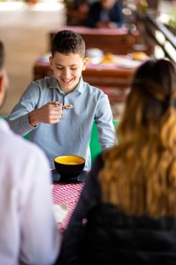 Genç çocuklar güneşli bir bahar ya da sonbahar günü ebeveynleriyle bir dağ restoranının terasında öğle yemeği yiyorlar.. 