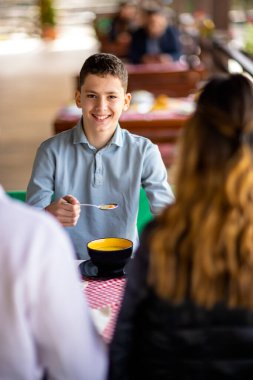 Genç çocuklar güneşli bir bahar ya da sonbahar günü ebeveynleriyle bir dağ restoranının terasında öğle yemeği yiyorlar.. 