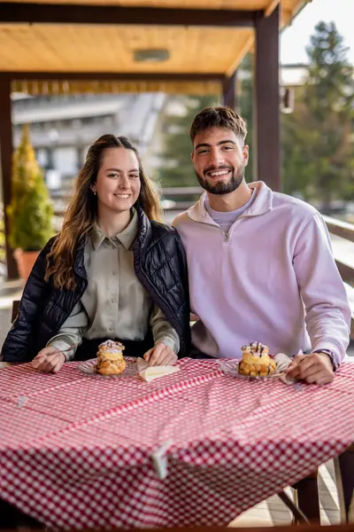 Genç bir çift, bir dağ restoranının terasında krema dolu profiterollerin tadını çıkarıyor.