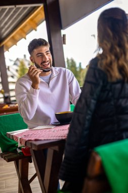 Genç çift, güneşli bir sonbahar ya da bahar günü birlikte bir dağ restoranının terasında öğle yemeği yiyorlar..