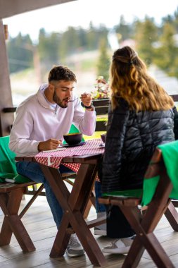 Genç çift, güneşli bir sonbahar ya da bahar günü birlikte bir dağ restoranının terasında öğle yemeği yiyorlar..