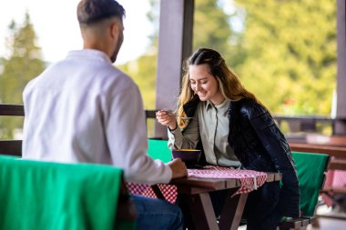 Genç çift, güneşli bir sonbahar ya da bahar günü birlikte bir dağ restoranının terasında öğle yemeği yiyorlar..