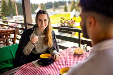 Genç çift, güneşli bir sonbahar ya da bahar günü birlikte bir dağ restoranının terasında öğle yemeği yiyorlar..