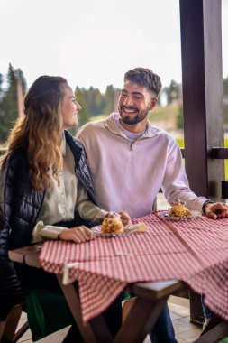 Genç bir çift, bir dağ restoranının terasında krema dolu profiterollerin tadını çıkarıyor.