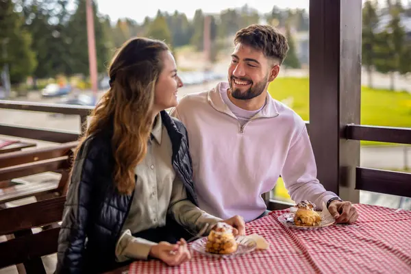 Genç bir çift, bir dağ restoranının terasında krema dolu profiterollerin tadını çıkarıyor.