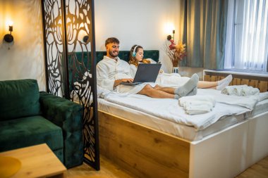 Modern bir çift, her biri kendi dijital dünyasına dalmış olarak yatakta dinlenir.. 