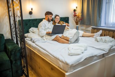 Modern bir çift, her biri kendi dijital dünyasına dalmış olarak yatakta dinlenir.. 