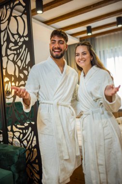 Bornoz giymiş bir çift otel odalarında dikiliyor.