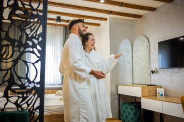 Bornoz giymiş bir çift otel odalarında dikiliyor.