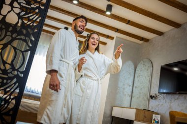 Bornoz giymiş bir çift otel odalarında dikiliyor.