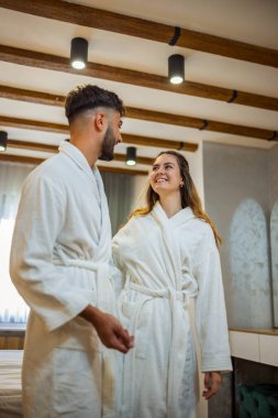 Bornoz giymiş bir çift otel odalarında dikiliyor.