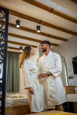 Bornoz giymiş bir çift otel odalarında dikiliyor.