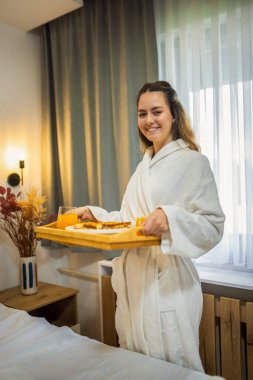 Kız arkadaşı ona kahvaltı hazırlarken, beyaz bornozlu genç adam yatakta gülümsüyor..