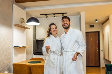 Bornoz giymiş bir çift otel odalarında dikiliyor.