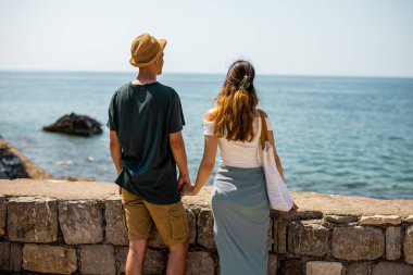 Genç bir çift, yaz tatili boyunca tarihi bir şehrin antik taş duvarlarında el ele tutuşuyor. Manzara arkadan geliyor..