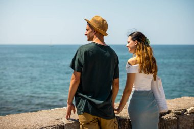 Genç bir çift, yaz tatili boyunca tarihi bir şehrin antik taş duvarlarında el ele tutuşuyor. Manzara arkadan geliyor..