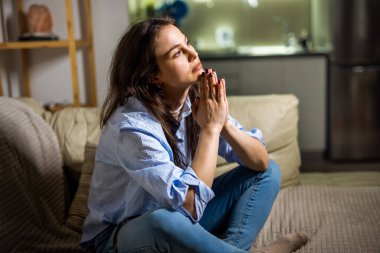 Oturma odasında oturan genç bir kadın üzgün ve duygusal olarak şaşkın bir şekilde depresyon anını canlandırıyor..