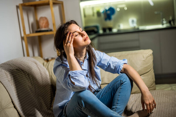 A young woman is sitting in her living room looking sad and emotionally overwhelmed, portraying a moment of depression.