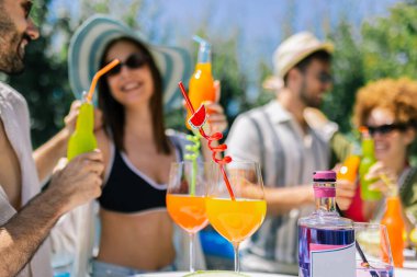 Bir grup genç havuz başında dans ediyor ve eğleniyor, pipetlerle renkli kokteyller içiyor, mayo, şapka, güneş gözlüğü takıyor ve ananas ve kavun gibi taze meyvelerle dolu bir masa hazırlıyorlar..