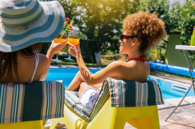 Mayolu iki kız arkadaş havuz kenarında eğleniyor, renkli kokteyller içiyor ve güneşli, neşeli bir yaz anının tadını çıkarıyor..