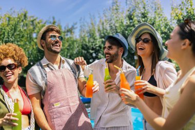  Canlı bir grup genç dans ediyor ve havuz başında eğleniyor, pipetle renkli kokteyller içiyor, mayo, şapka ve güneş gözlüğü takıyor.