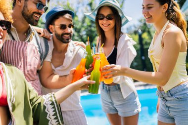 Canlı bir grup genç havuz kenarında renkli kokteyllerle dans ediyor, mayo, şapka ve güneş gözlüğü takıyor..