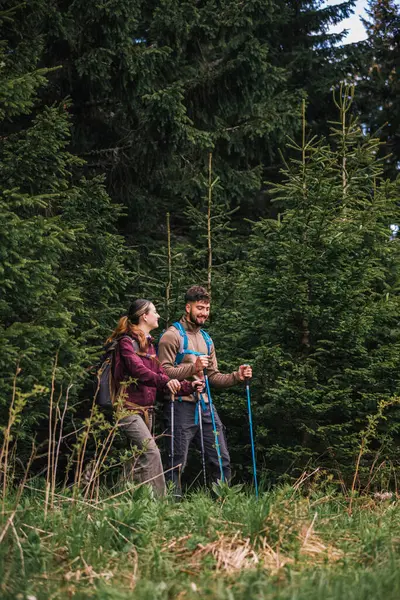 Sırt çantaları, yürüyüş direkleri ve yürüyüş elbiseleriyle donatılmış genç bir adam ve kadın yoğun çalılarla çevrili engebeli bir dağ yolunda dikkatle ilerliyorlar.. 