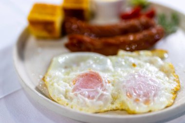 Izgara sosis, krema, ekmek, taze domates ve salatalık ile servis edilen yumurta klasik, doyurucu bir kahvaltı tabağı..